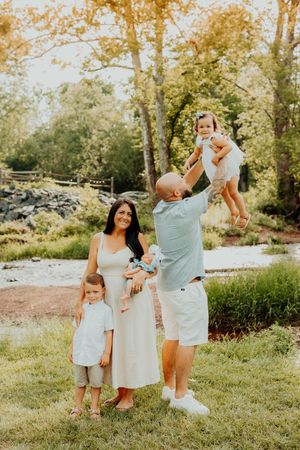 Family of four dressed in soft neutral colors poses together outdoors during golden hour in a natural park setting.
