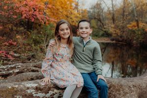 A couple sits together enjoying a peaceful autumn day by a pond surrounded by colorful fall foliage.