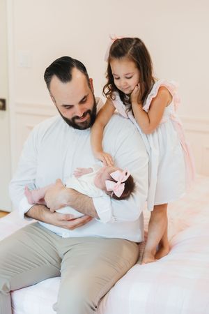 Family shares tender moment together on white couch as they welcome new baby wearing pink bow.