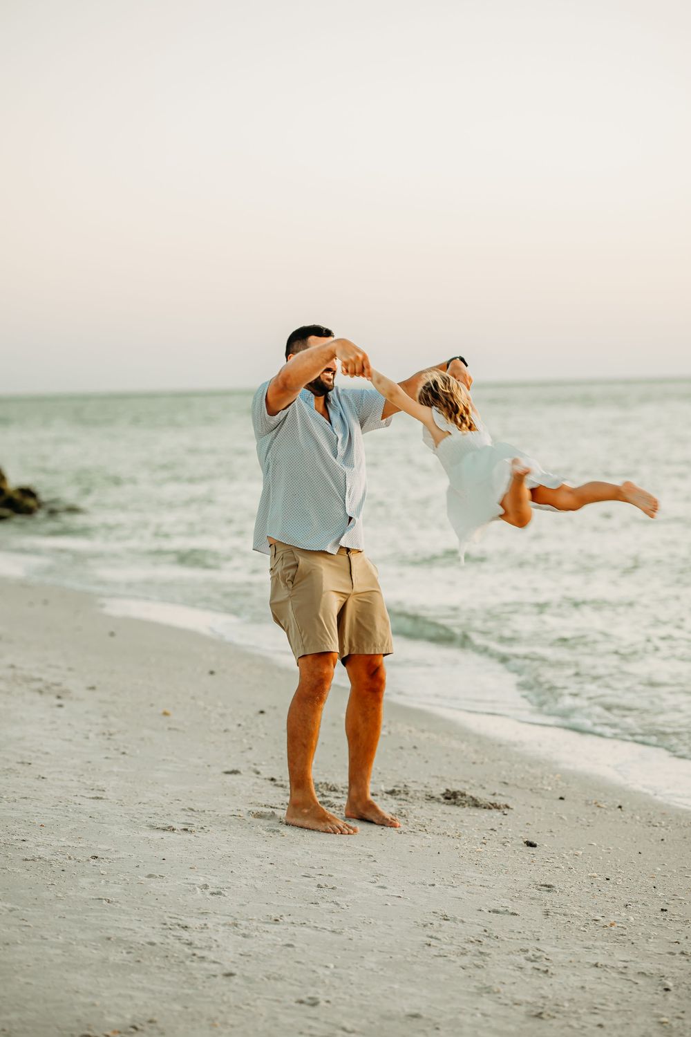 having fun on beach at sunset as man swings woman around.