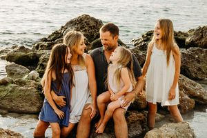 Family of five sitting together on rocky beach during sunset photo session.