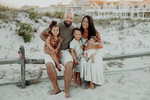 Loving family shares tender moments together while seated on wooden walkway at sunset along sandy beach dunes.