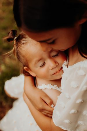 A tender moment between parent and child embracing in white dresses against a soft blurred background.