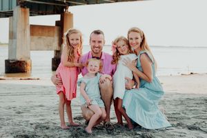 A happy family in coordinating pink and blue outfits poses together on a beach at sunset.