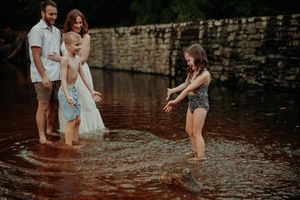 Family splashes and plays together in shallow creek water on a sunny summer day.