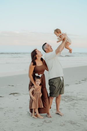Family enjoying a sunset moment together at the beach in coordinated brown and neutral outfits.