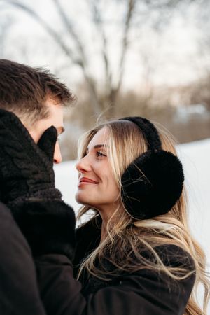 A couple in black winter coats share intimate moments in a snowy outdoor setting.