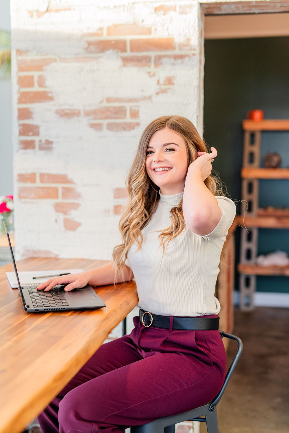 Medical professional working on laptop at wooden desk with exposed brick wall background.
