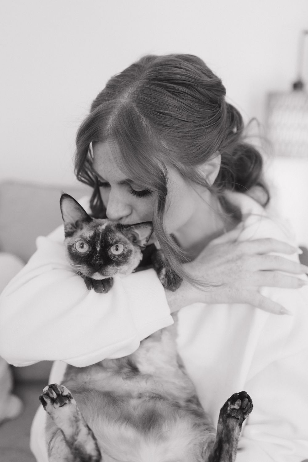 Sweet moments shared between a person in white and a Siamese cat in black and white photography.