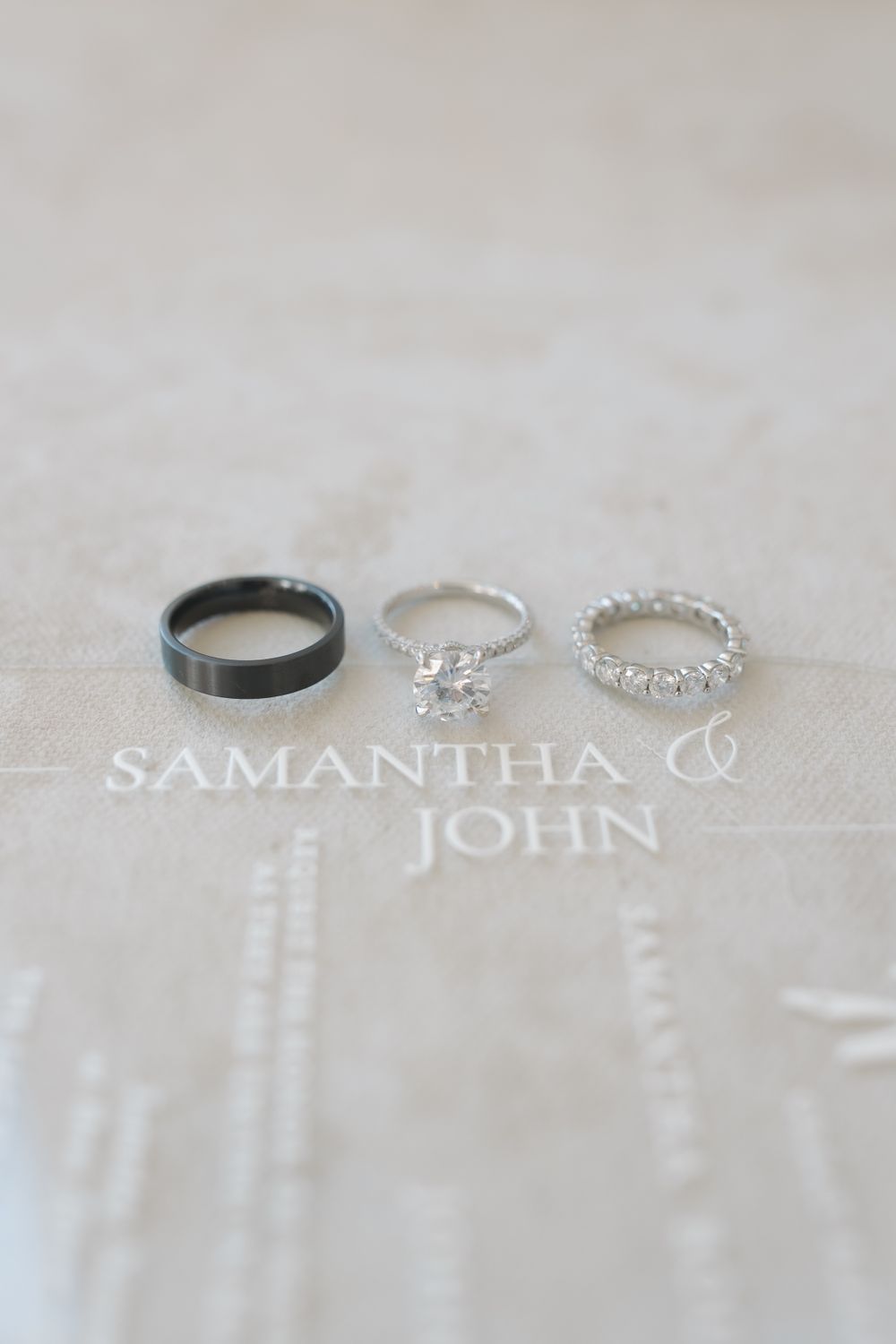 Three wedding rings and names Samantha & John displayed on white fabric.