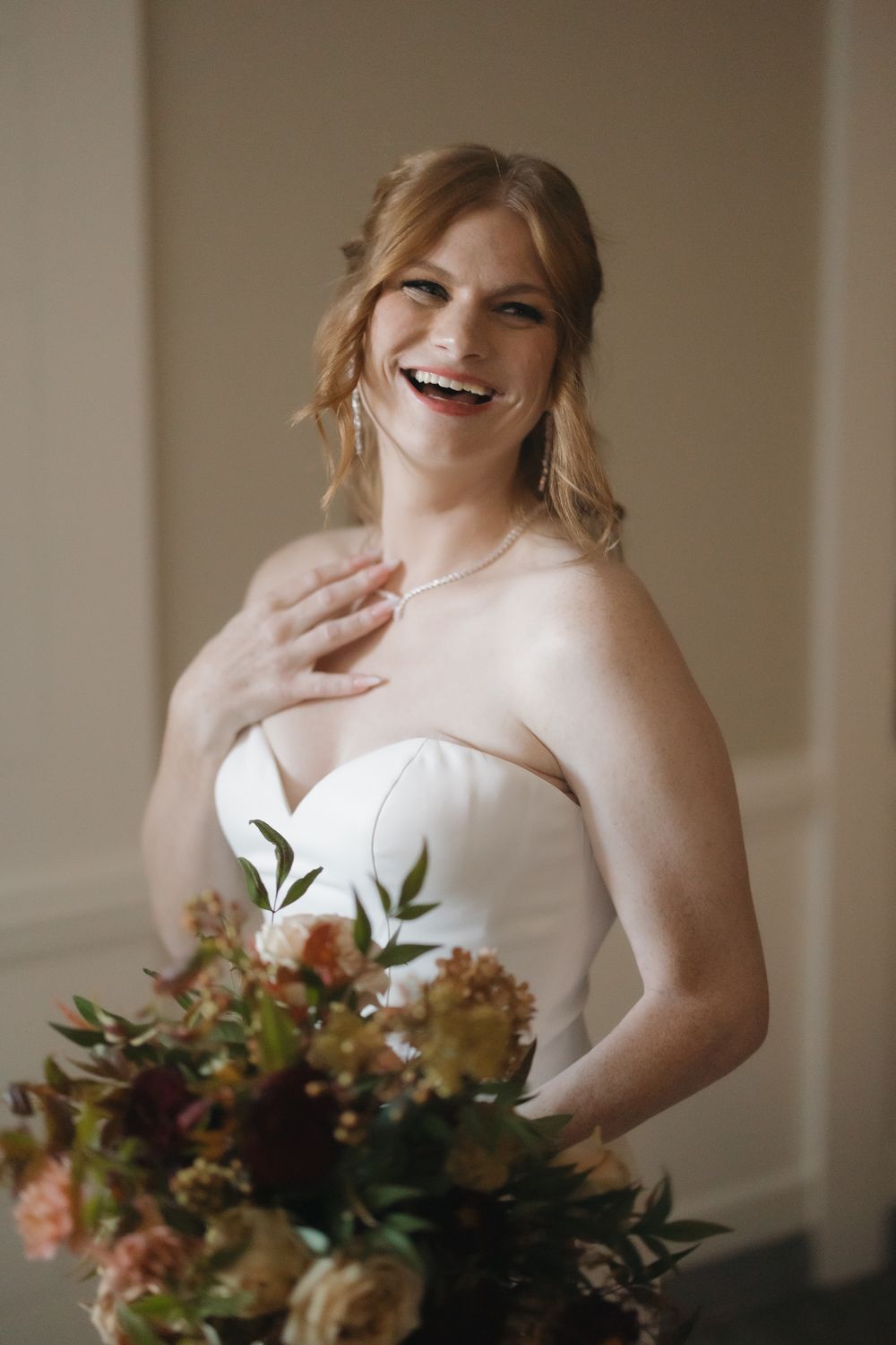 A wedding bouquet with fall-colored flowers complements a strapless white bridal gown.