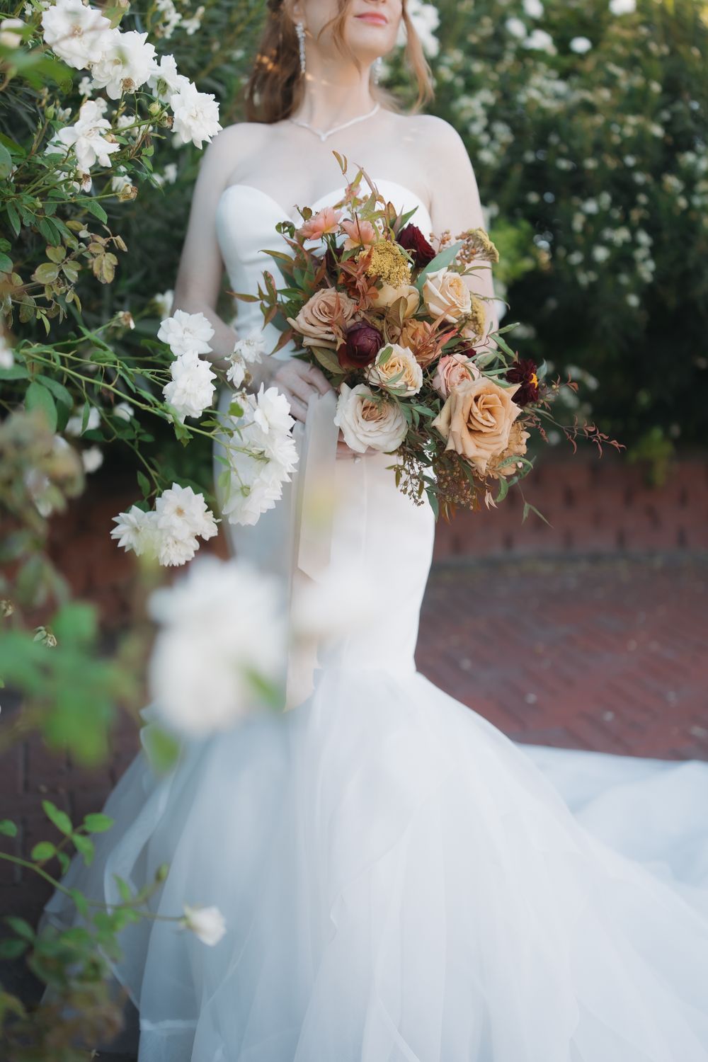 A strapless wedding gown is complemented by a peach and burgundy floral bouquet.