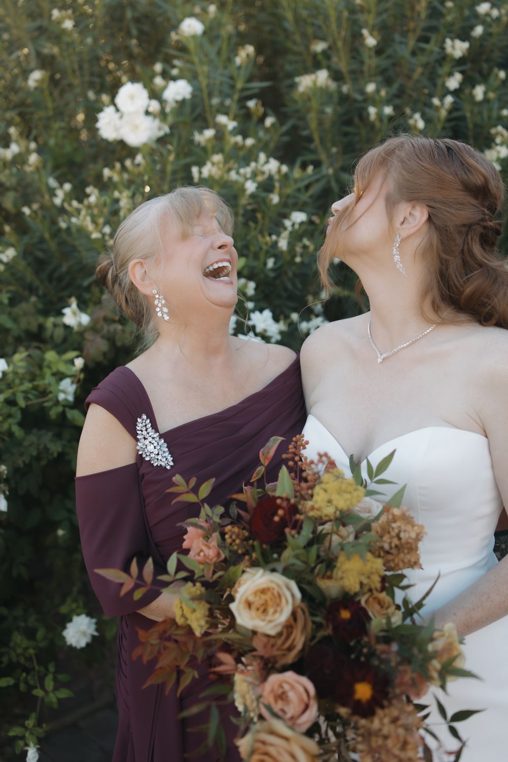 Two people share a joyful moment surrounded by white flowers and autumn-colored bouquets.