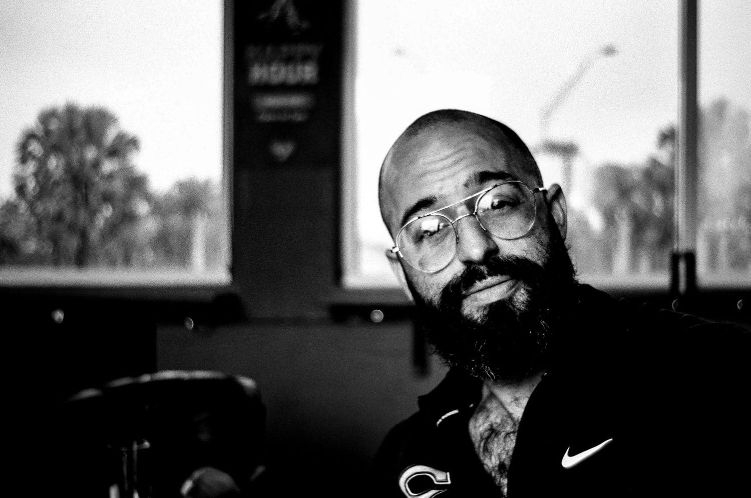 A black and white portrait of someone wearing glasses and a Nike shirt in subdued lighting.