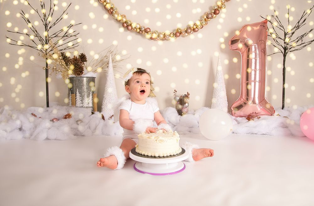 First birthday cake smash photo session in a magical winter wonderland setting with twinkling lights and rose gold decorations.