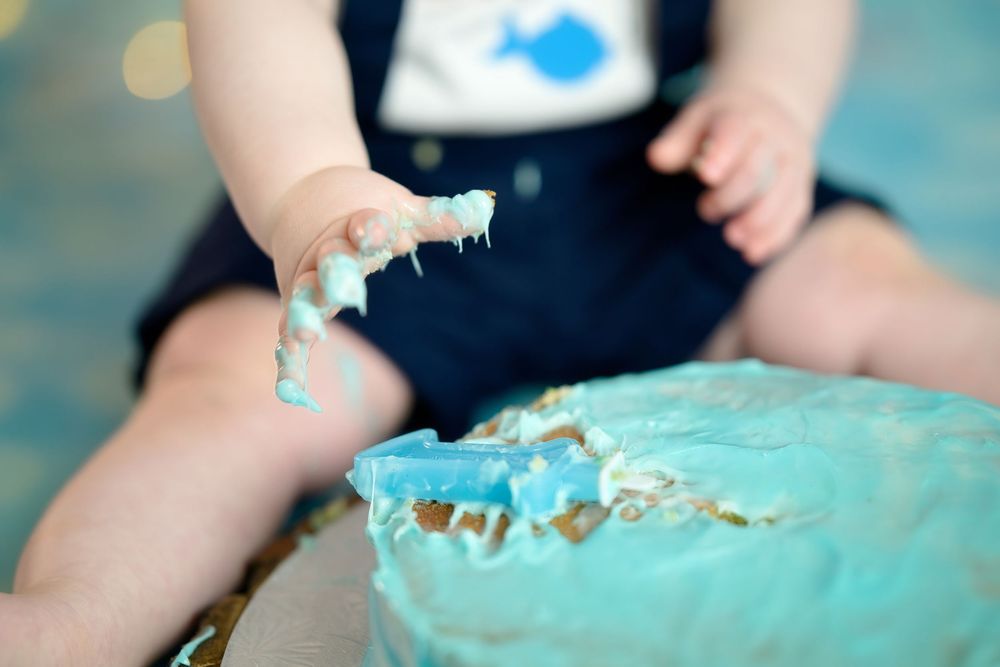 Close-up shots of small hands smashing into a turquoise birthday cake during a cake smash photo session.