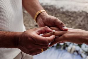 Close-up of a man placing a diamond engagement ring on a woman's finger during an outdoor wedding ceremony.