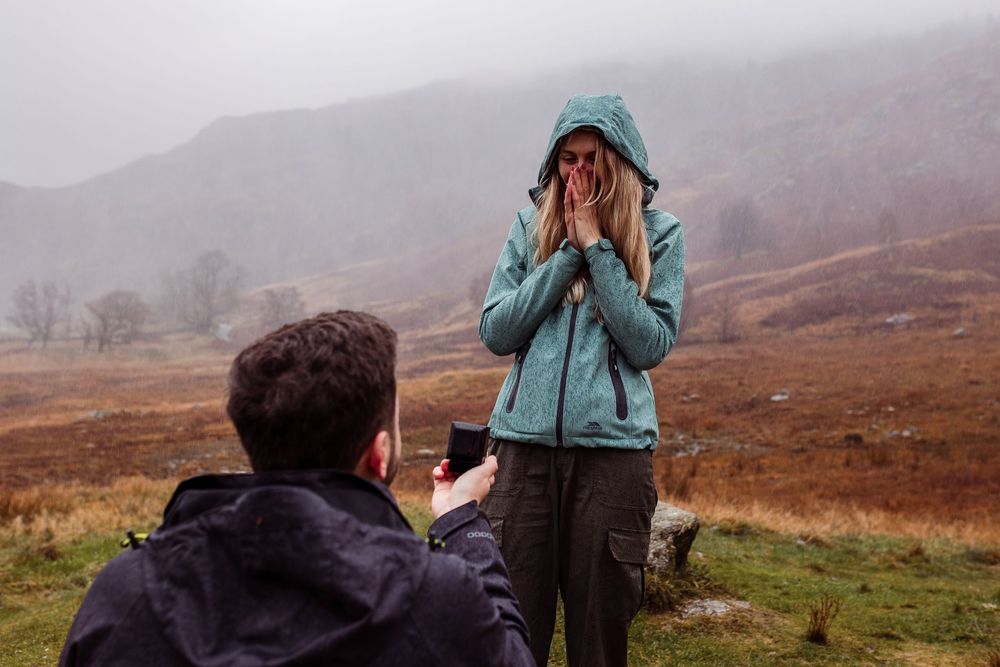 A person in a teal jacket takes photos while hiking through misty Scottish Highlands in autumn.