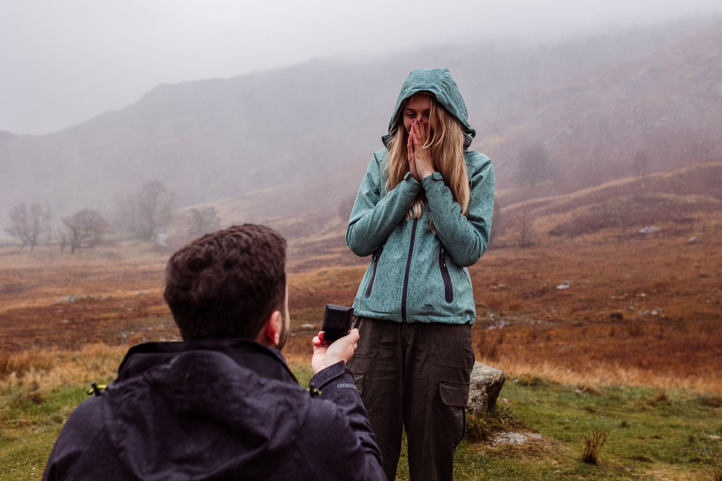 A person in a teal jacket takes photos while hiking through misty Scottish Highlands in autumn.