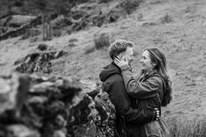 A couple embraces on a grassy hillside slope in black and white.