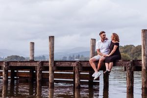A couple sits together on a wooden pier overlooking the water during an overcast day.
