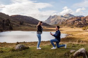 Silhouettes of a couple in the Scottish Highlands proposing by a scenic mountain lake during golden hour.