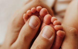 A close-up of a parent gently holding tiny newborn baby feet in their hands.