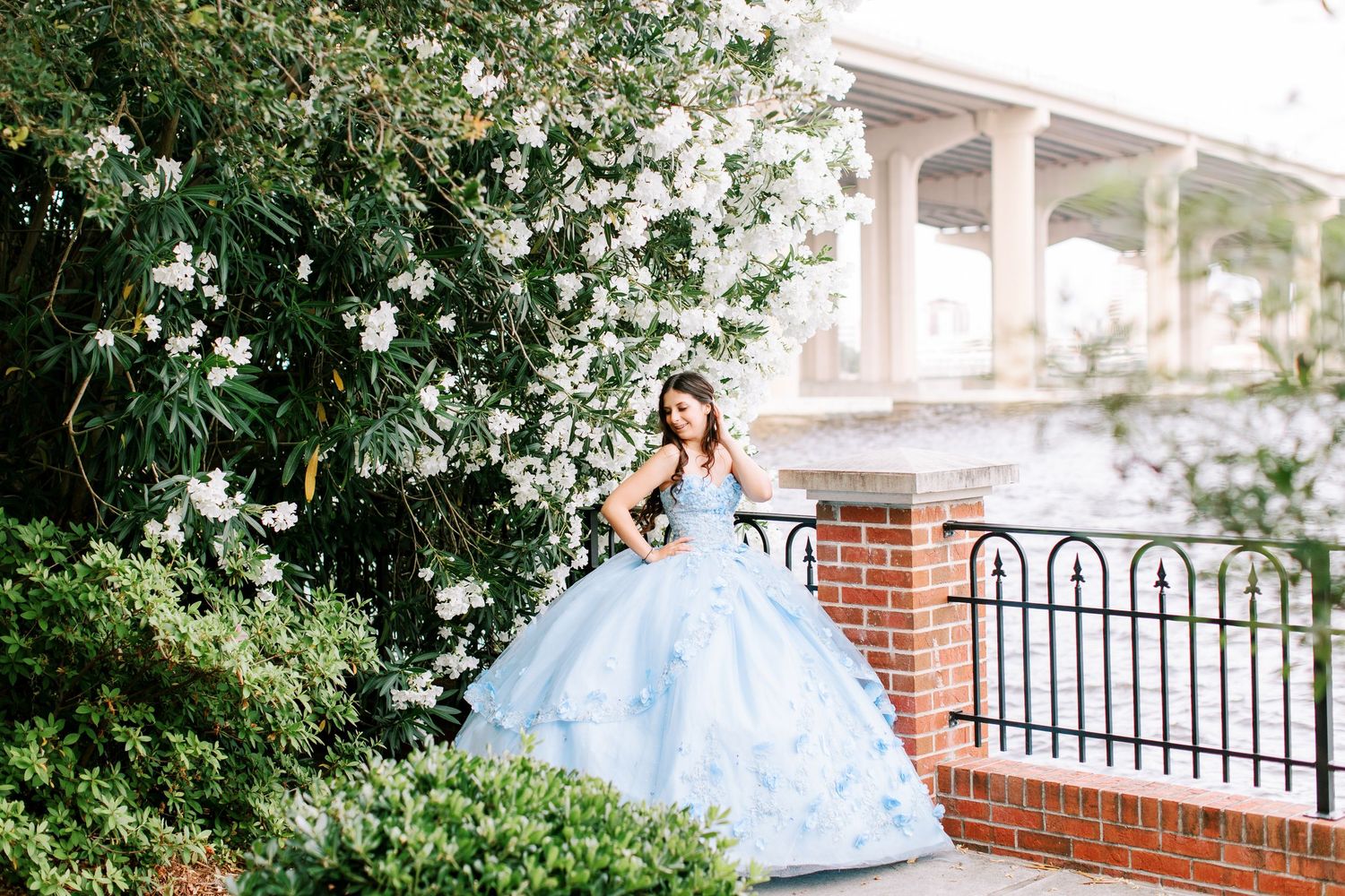 A series of outdoor Quinceañera portraits featuring a light blue ballgown against a backdrop of white flowers and brick walls. at the cummer