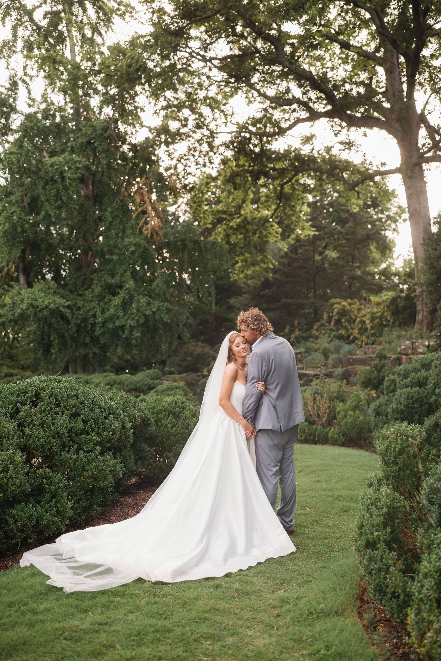 A couple in wedding attire embraces on a grassy hillside during golden hour.