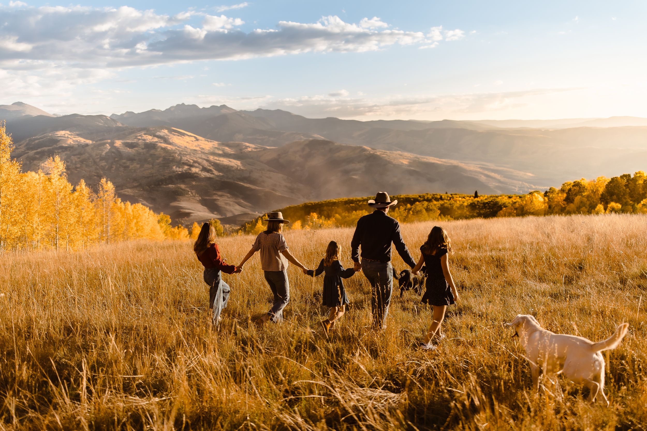 Family of five walking candidly in a Vail, Colorado field with golden hour mountains sunset