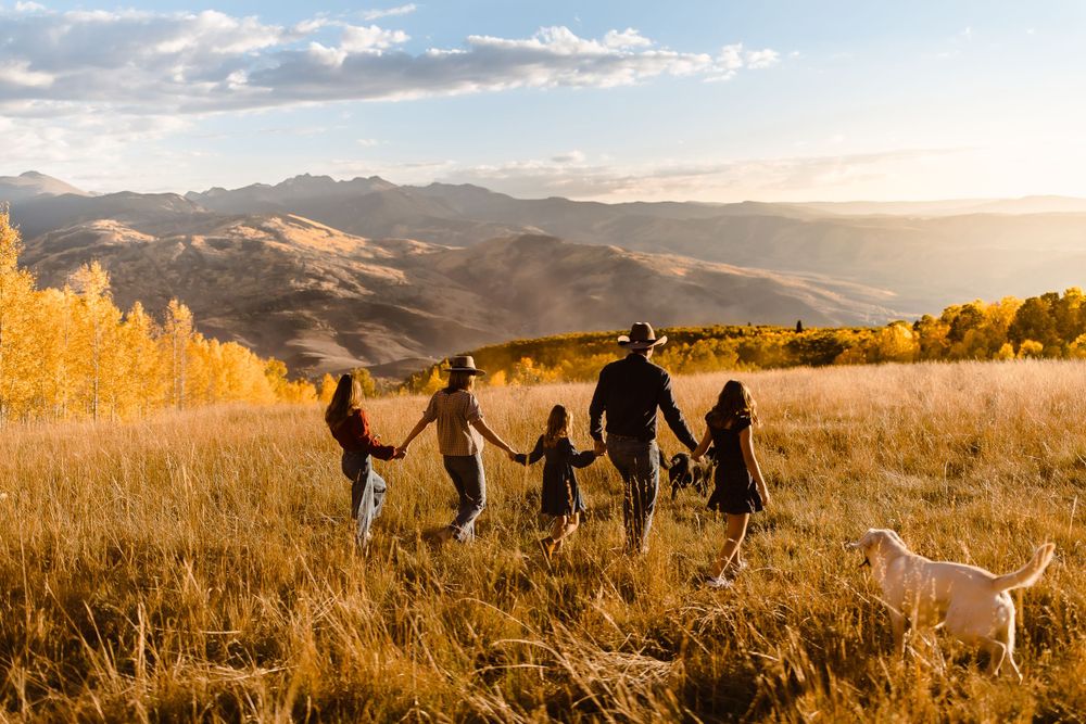 Family of five walking candidly in a Vail, Colorado field with golden hour mountains sunset