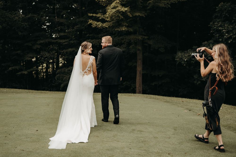 Photographer captures bride and groom holding hands on golf course surrounded by tall evergreen trees.