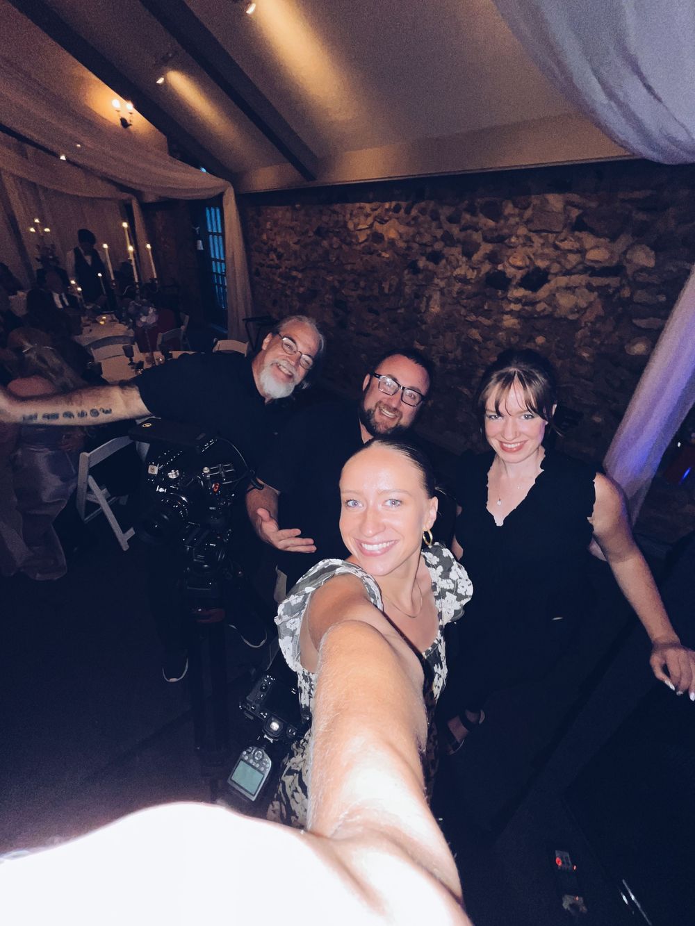 Wedding videography team taking a fun selfie together inside a rustic stone-walled reception venue.