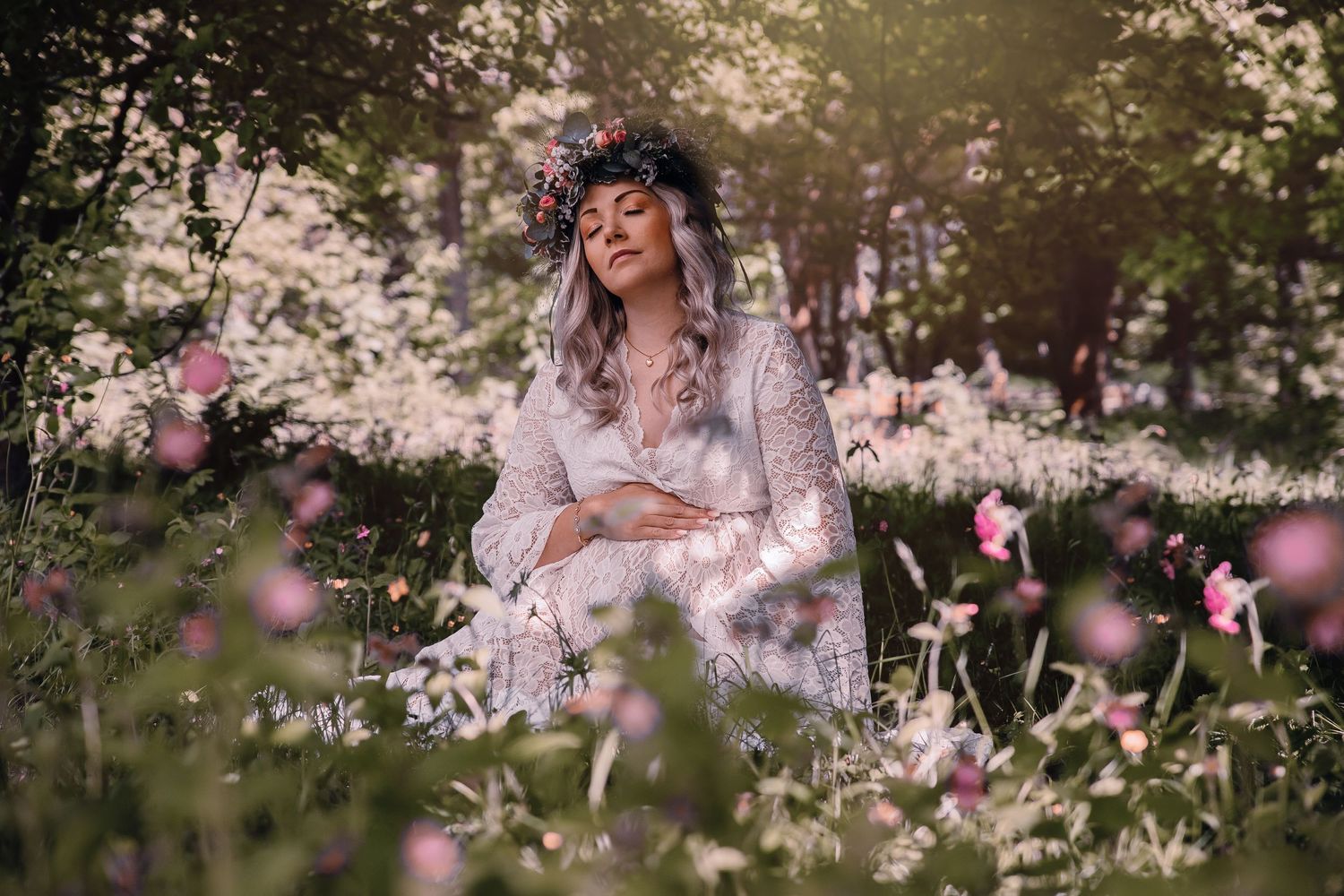 Ethereal figure in lace dress sits among blooming wildflowers at sunset in dreamy outdoor setting.