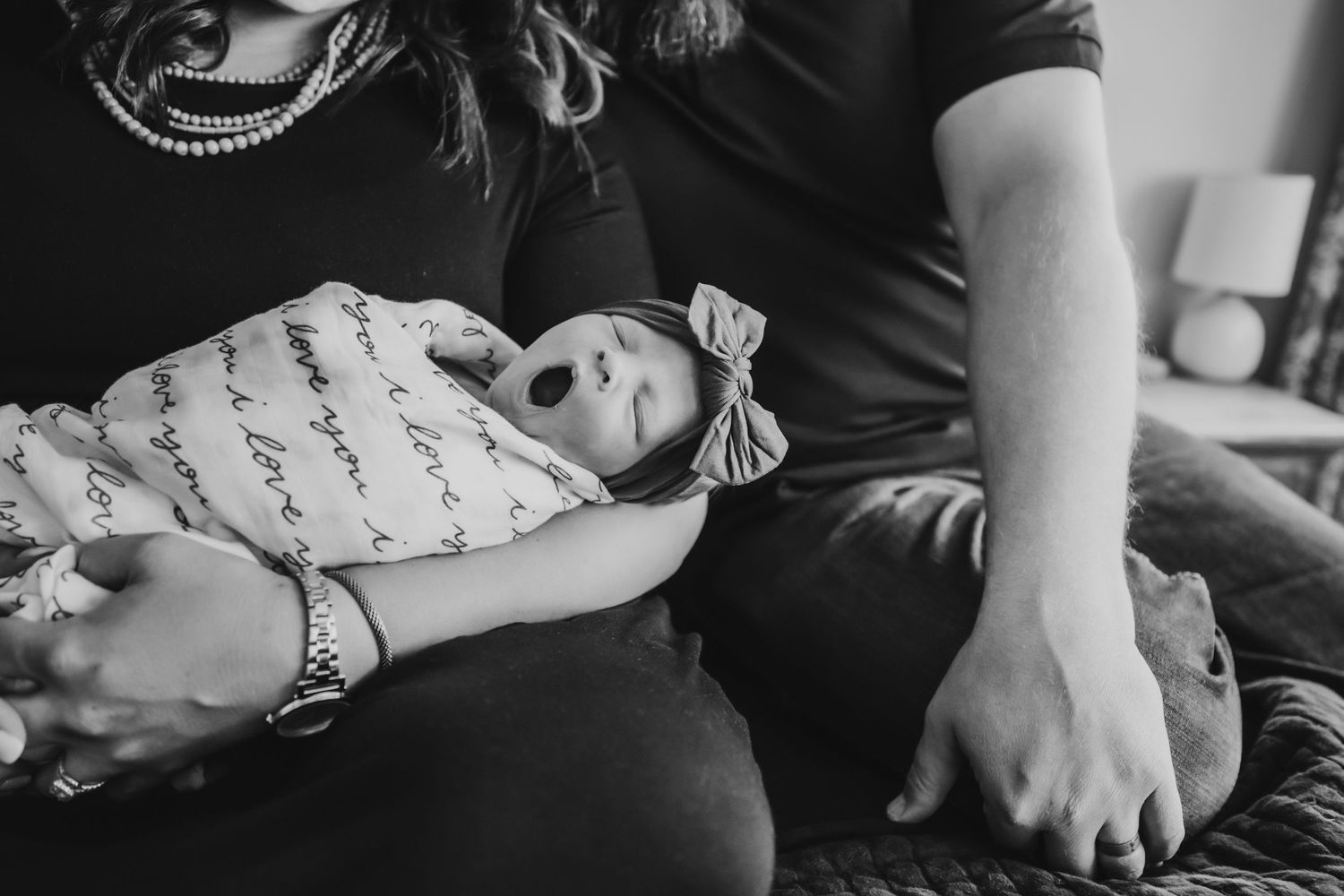 Newborn baby with bow on her head yawning in mom and dad's arms in Dickson, TN