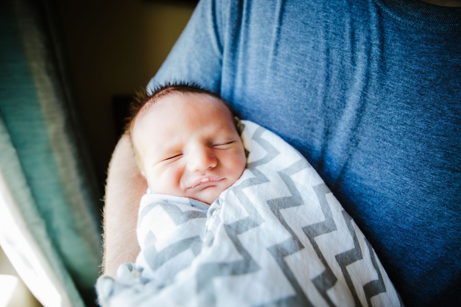 Newborn baby in white and grey blanket smiles in dad's arms in Dickson, TN