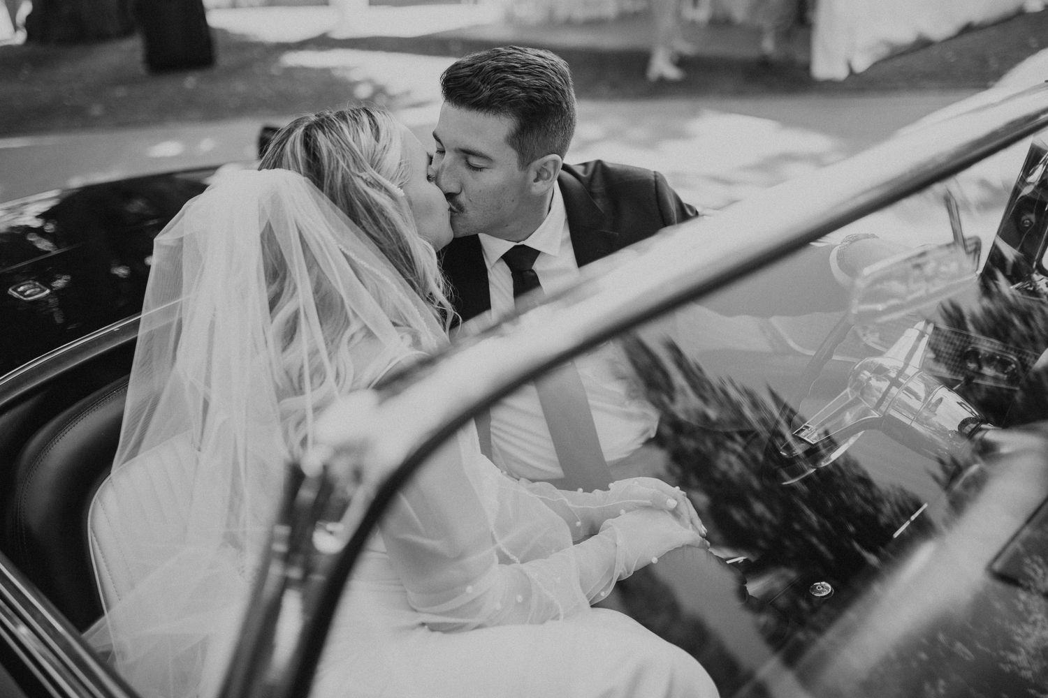 A romantic black and white wedding photo captured through a vintage car window.