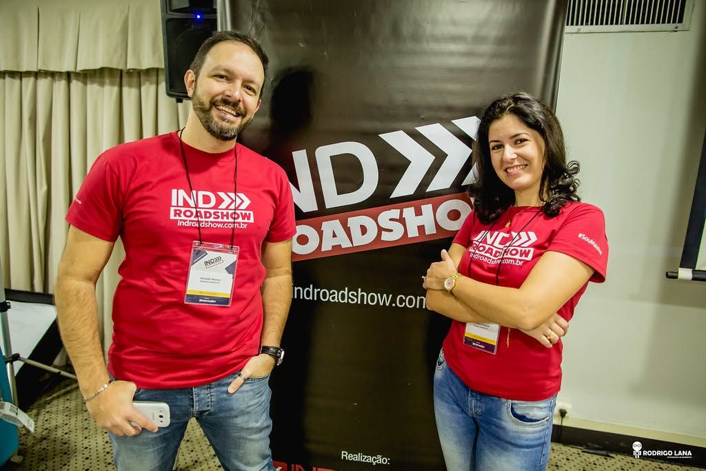 Two smiling people in red IND Roadshow t-shirts pose together at an IND Roadshow event booth.