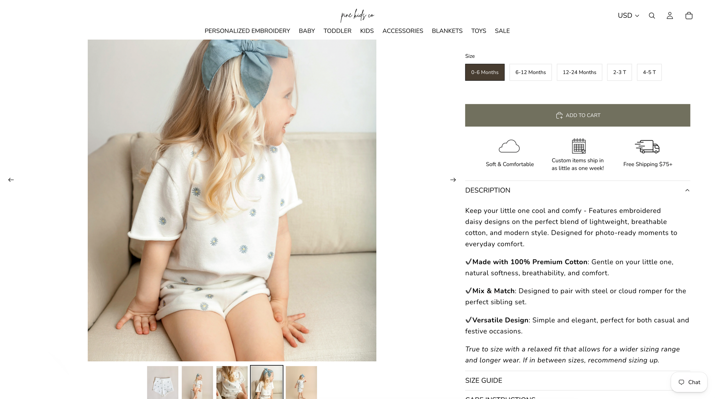 Young girl in white floral cotton top and shorts set, sitting on a couch, wearing a blue bow hair clip.