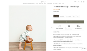 Baby wearing a striped Summer Knit Top in Steel Stripe, seated on a wooden stool against a white background.