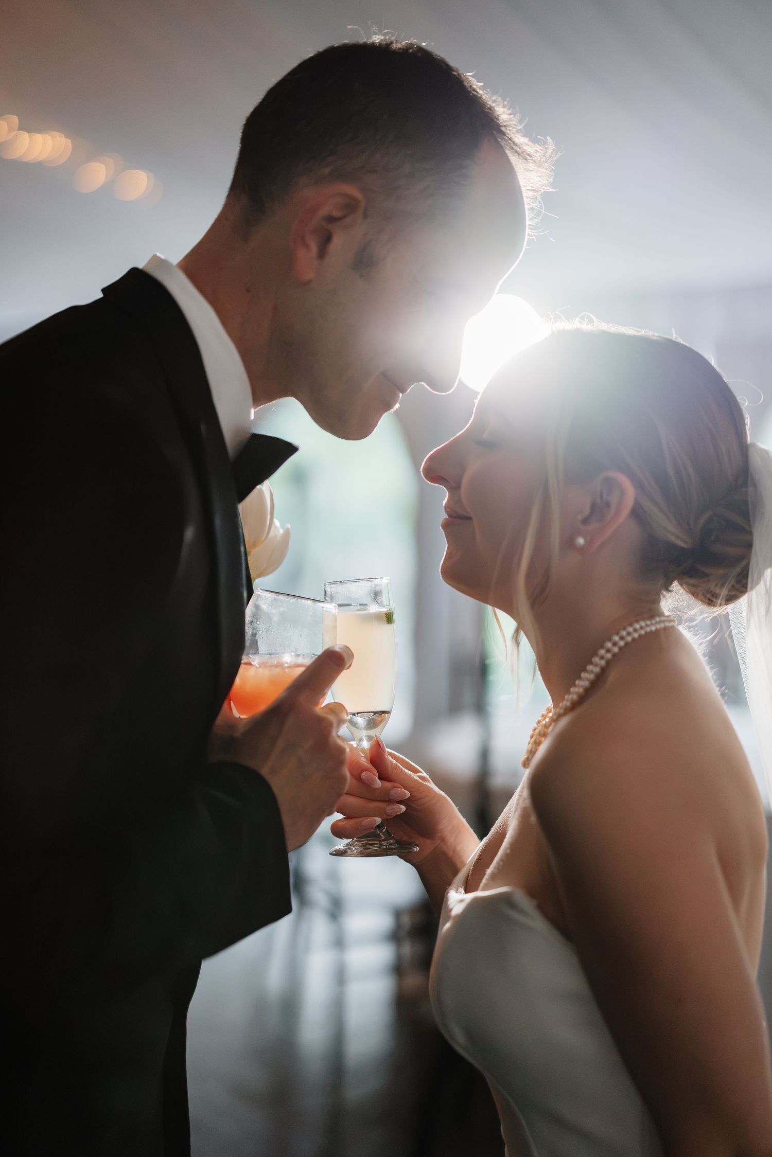 Bride and groom touch foreheads romantically while holding cocktail glasses at their wedding.
