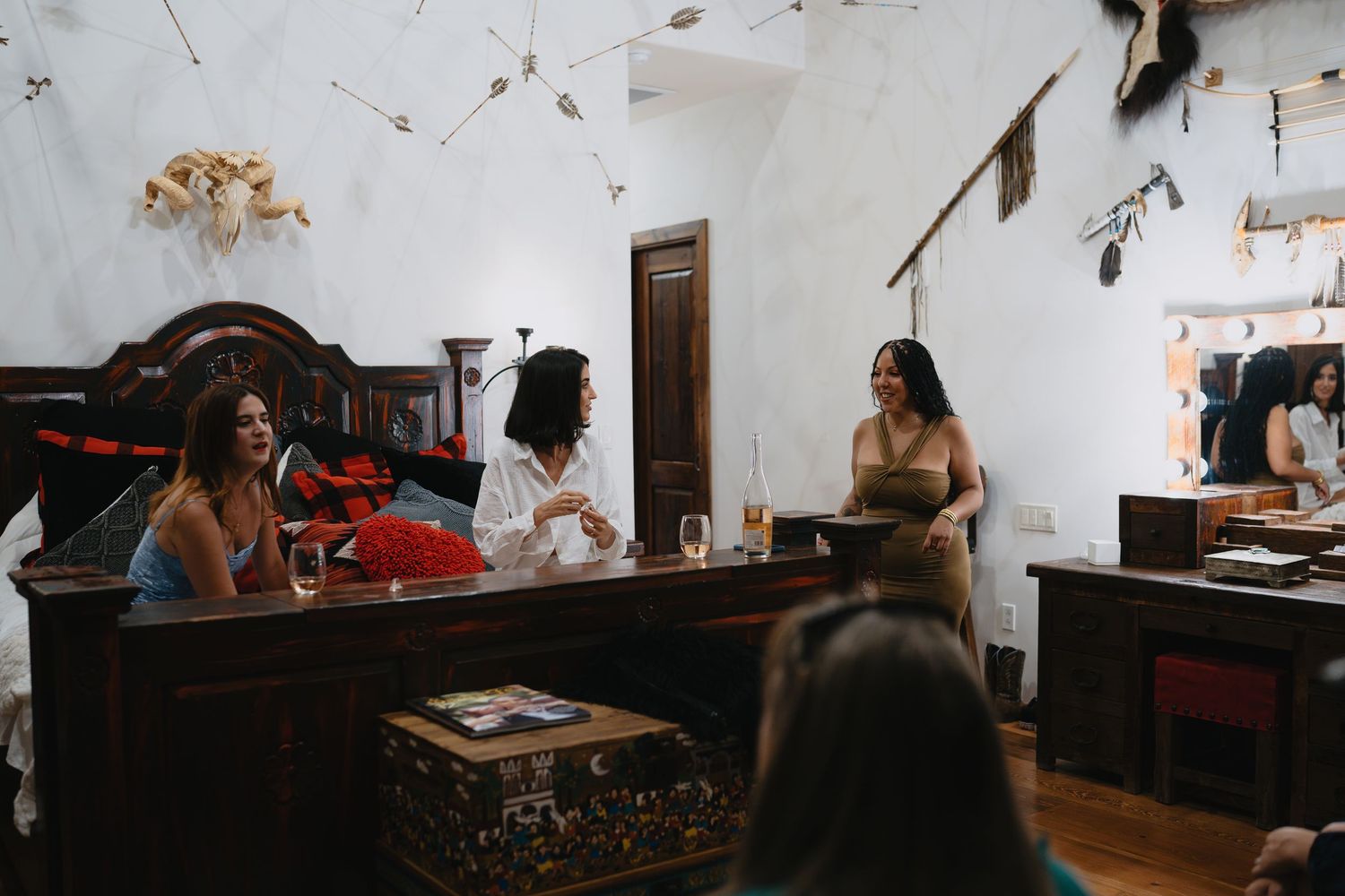 Women socializing in a rustic, eclectic room with vintage furniture and decorative wall art.