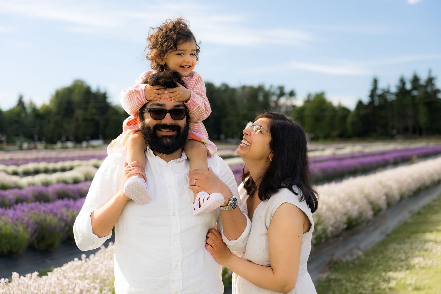 Happy family with young child on father's shoulders enjoying a sunny day in a colorful lavender field.