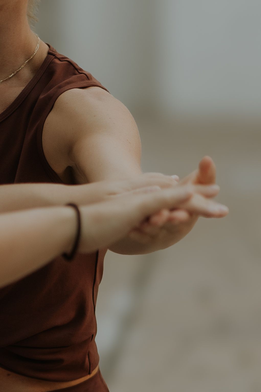 A woman in a brown sleeveless top stretches her arms forward with hands clasped during a yoga or dance practice.