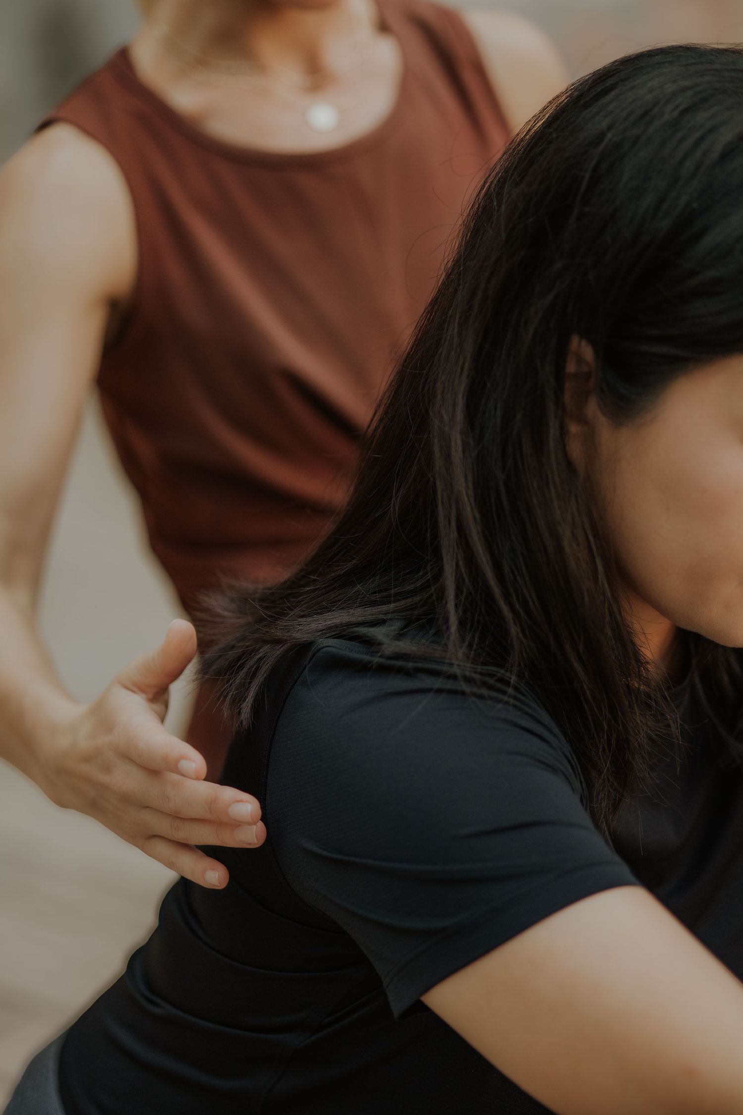 Yoga instructor in brown top adjusting student's posture during a yoga class session.