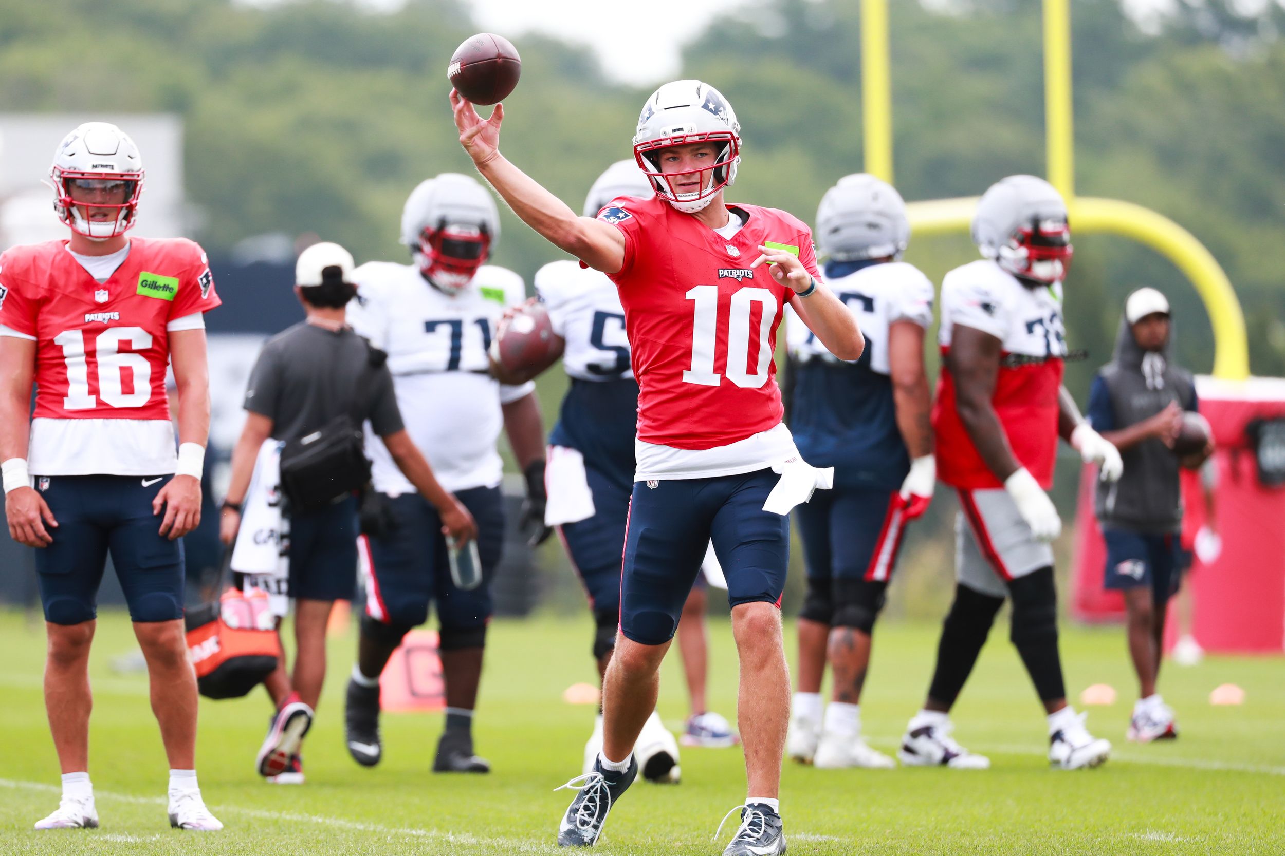NFL player wearing number 10 red jersey throws football during New England Patriots training camp practice.