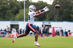 NFL player in Patriots uniform catching a football during outdoor practice on a green field.