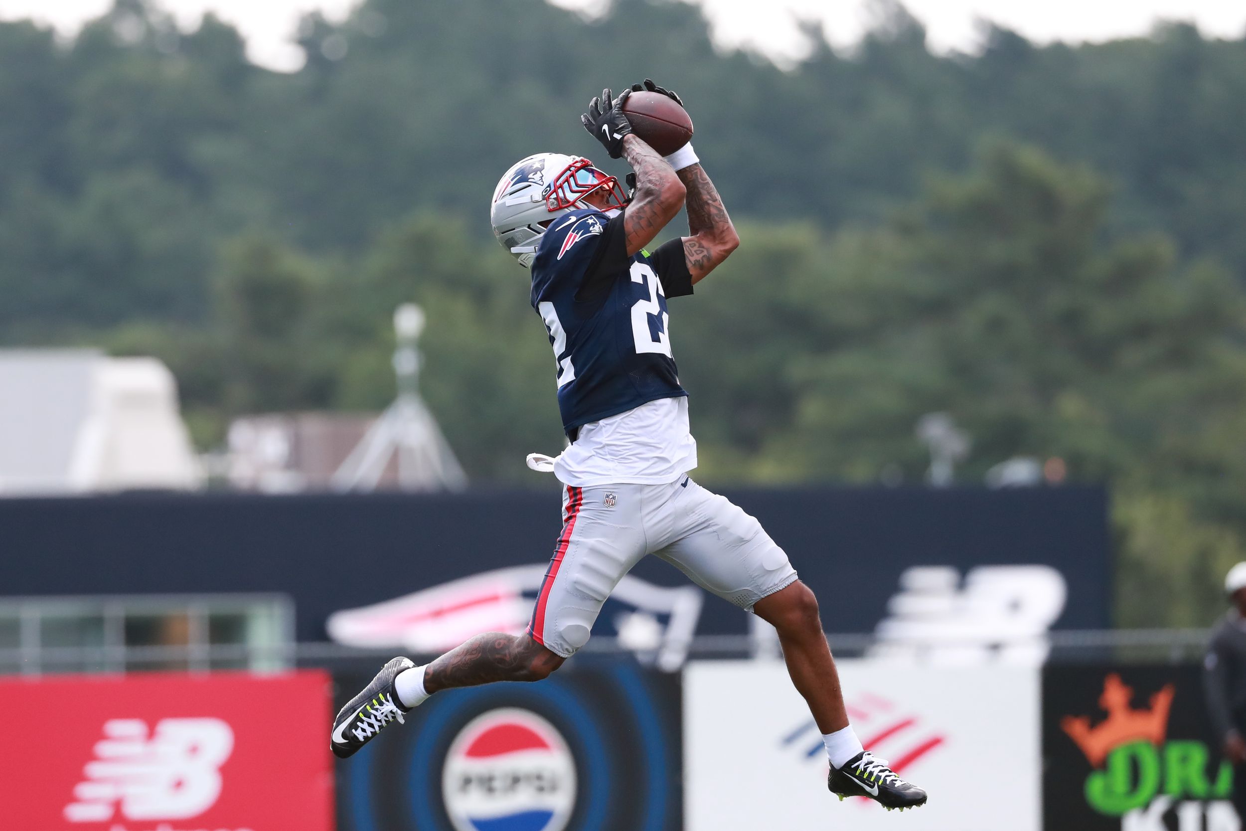 NFL player in Patriots uniform leaps to catch football during outdoor training camp practice.