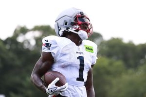 NFL player wearing number 1 jersey and red helmet holds football during New England Patriots training camp practice.