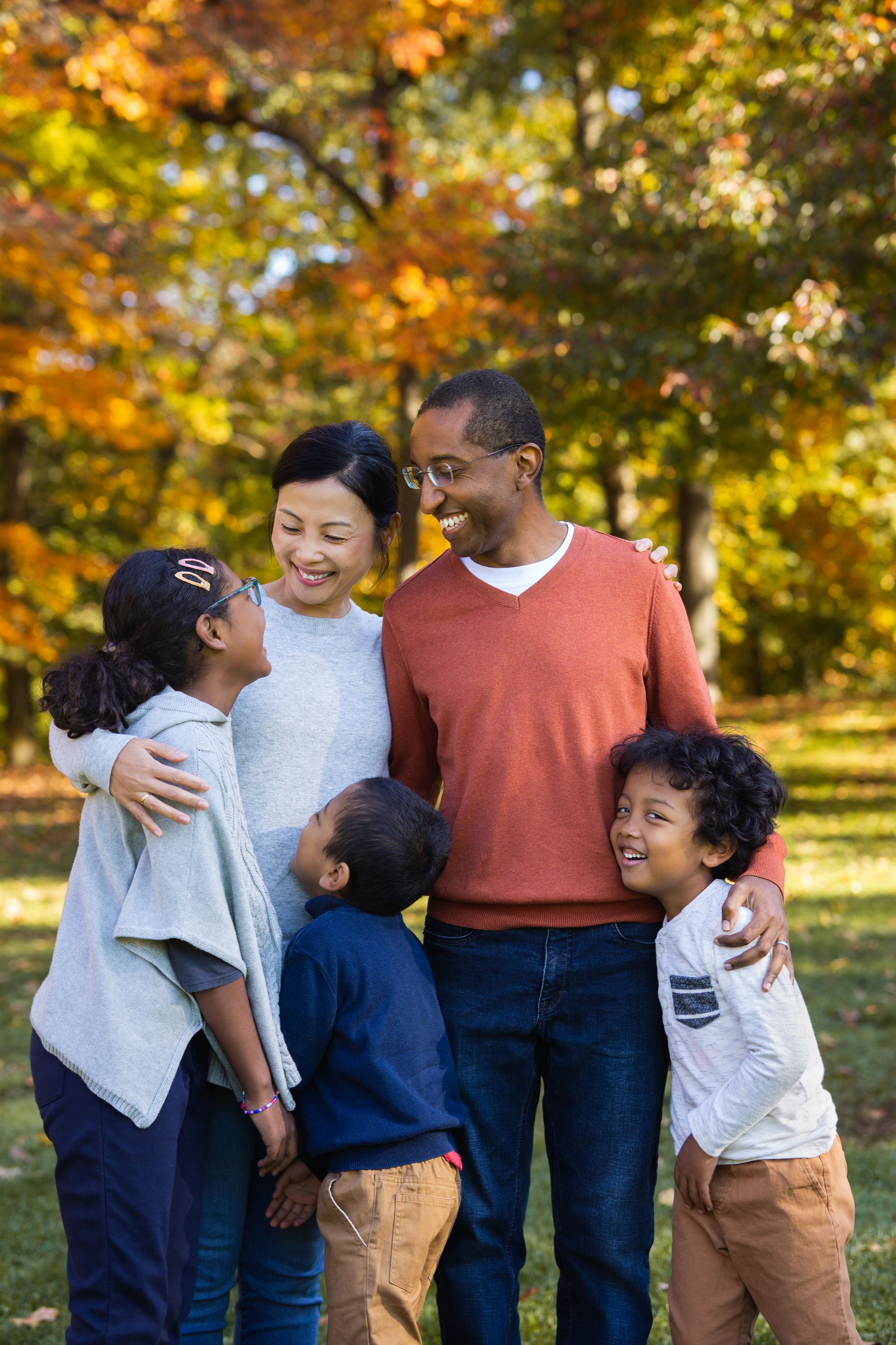 Happy multiracial family of five smiling together in a colorful autumn park setting.
